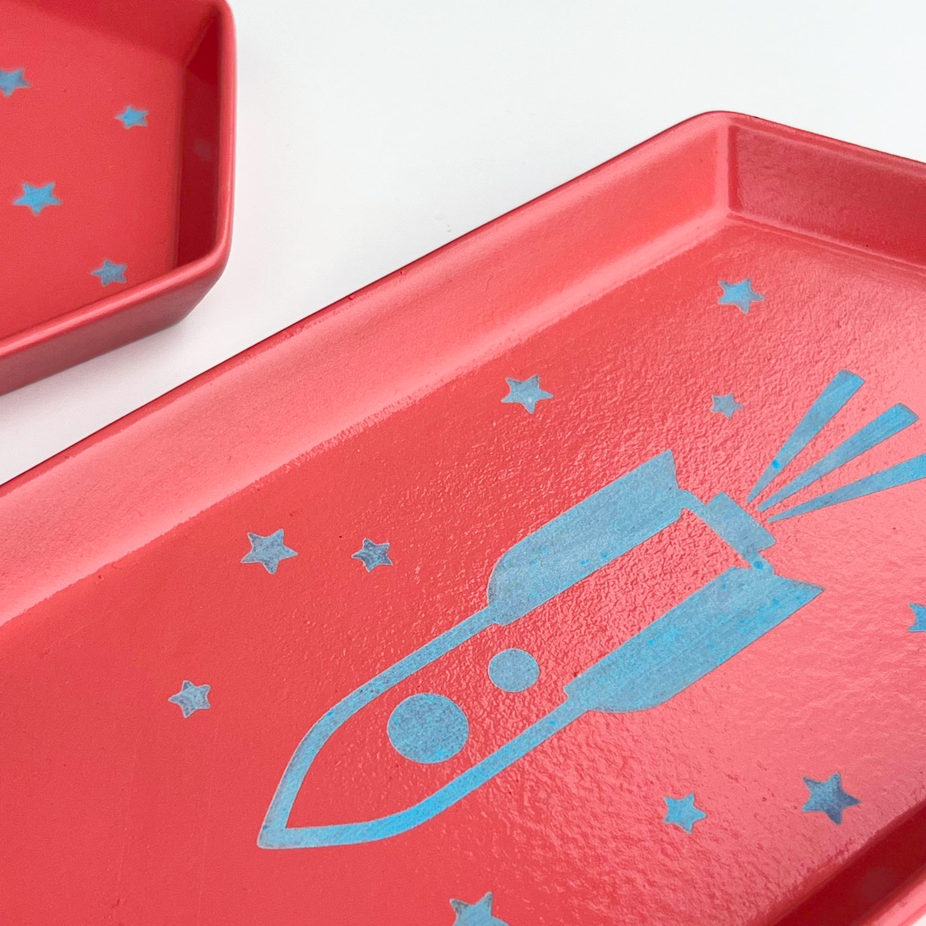 Red ceramic trinket trays with a light blue rocket and stars engraved through the glaze